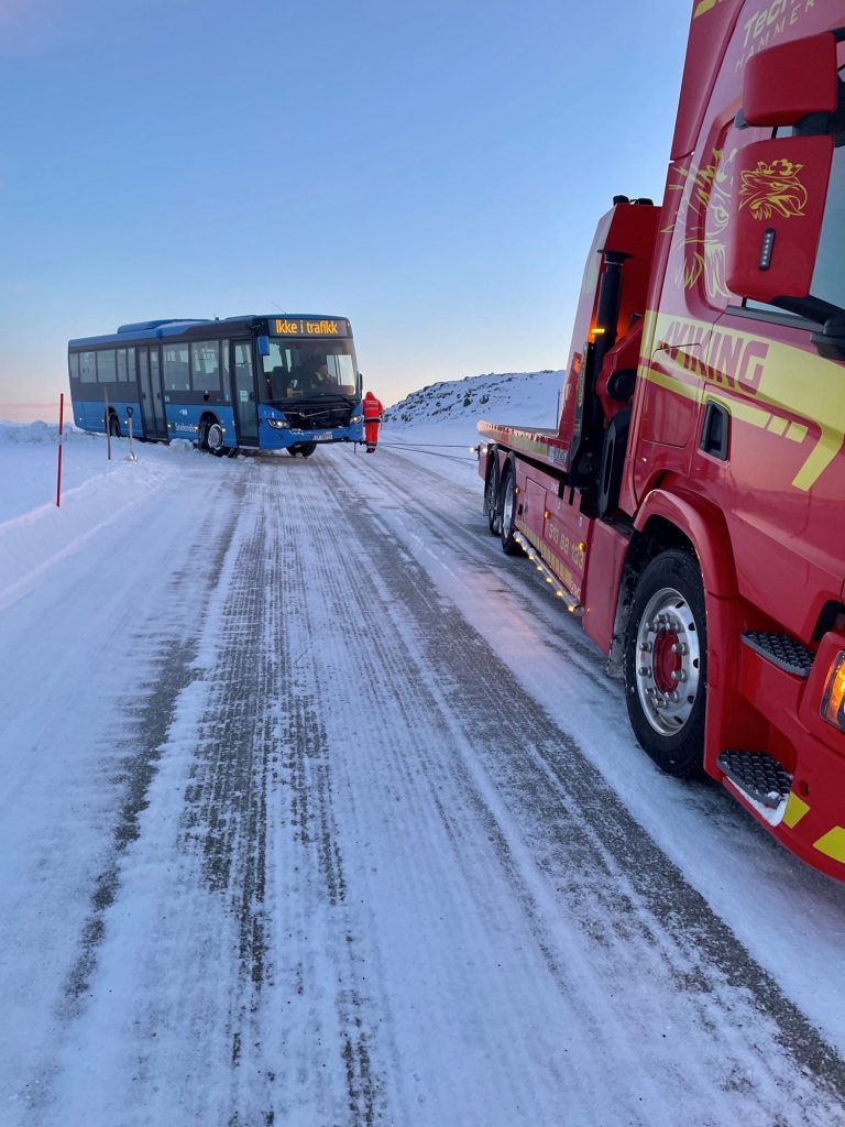 Redningsbil redder buss opp av veikanten.